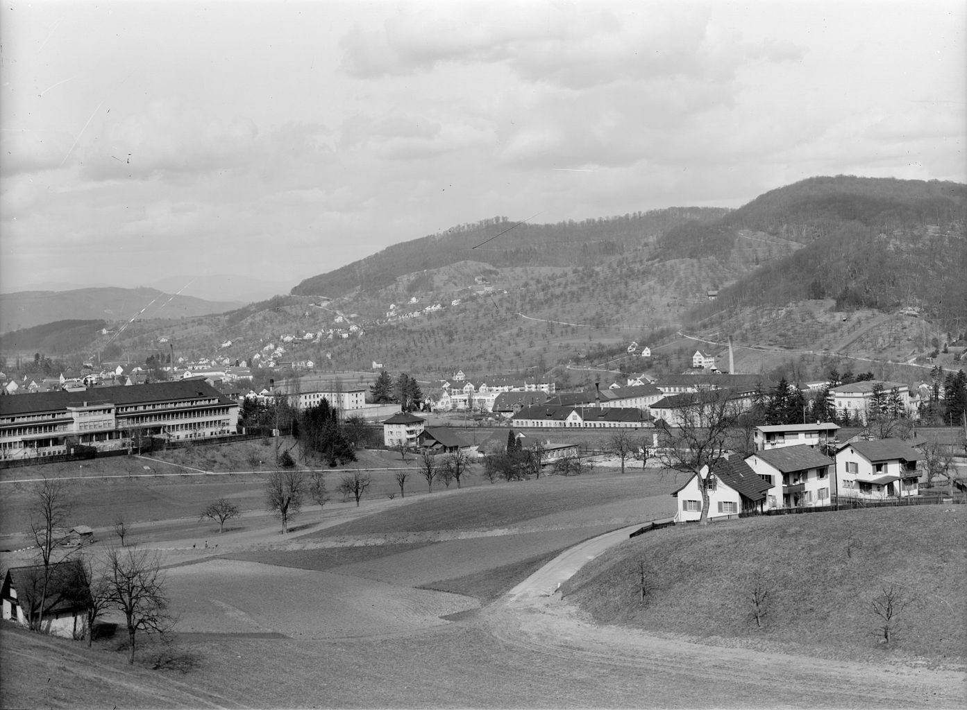 Blick vom Laubiberg Richtung Füllinsdorf. Heil- und Pflegeanstalt Hasenbühl (1934, links), Tierpark Weihermätteli im Vordergrund, Hufeisenförmiger Bau mit Ökonomiegebäude (nach dem Bahndamm, 1854, 1888, 1913) und Birmann-Spital (rechts, 1875), Liestal
